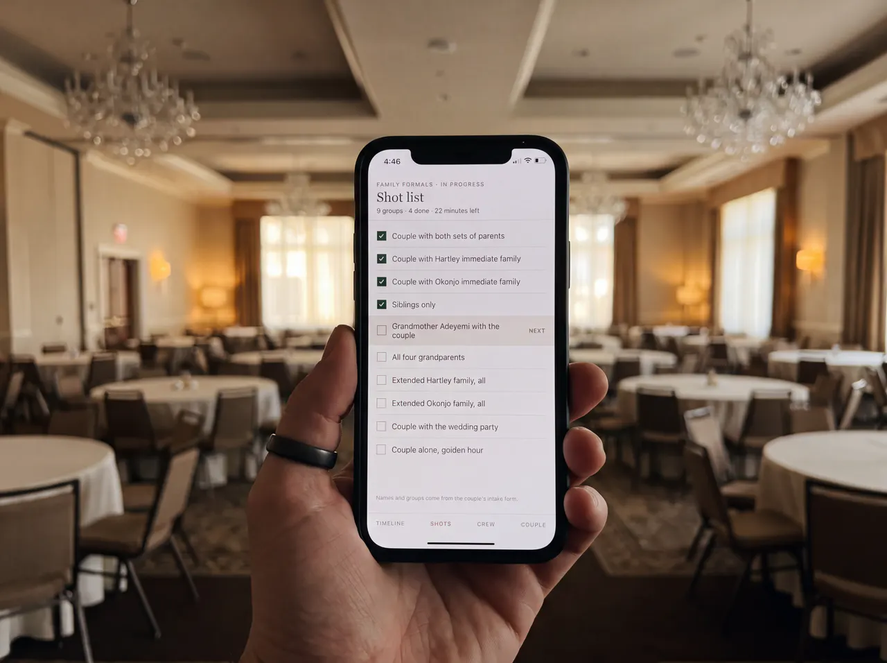 A hand holding a phone showing the shot list, in a ballroom set for dinner.